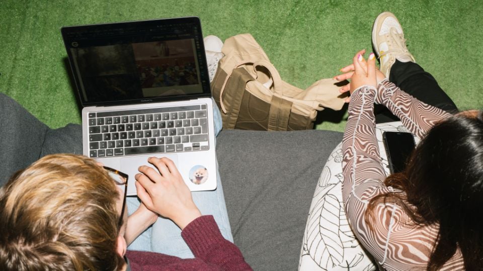 Two people sitting next to each other, one has a laptop.